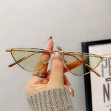 Gold cat-eye glasses held by a hand with a neutral background