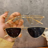 Gold cat-eye sunglasses held by a hand against a gray background